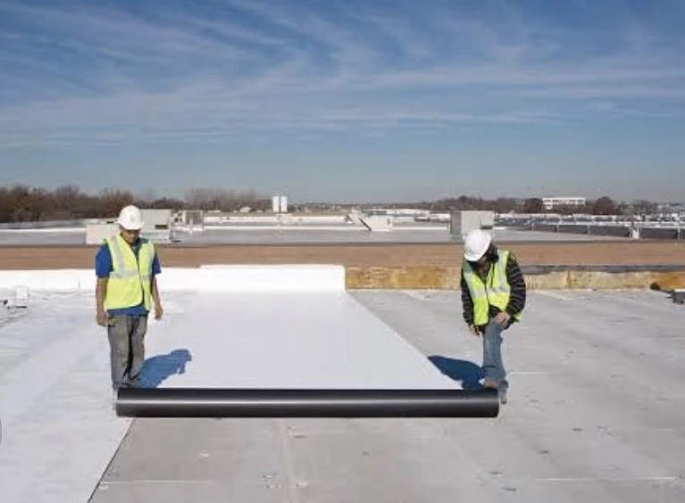 Nelson Roof Contracting crew unrolling white single-ply membrane on a commercial roof under a blue sky
